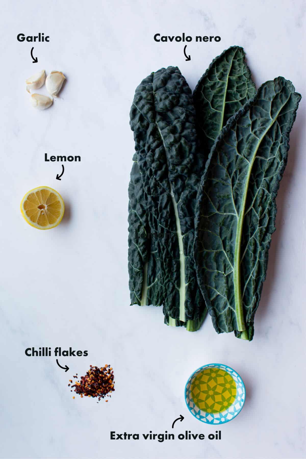 Ingredients to make cavolo nero with garlic and lemon laid out on pale background and labelled.