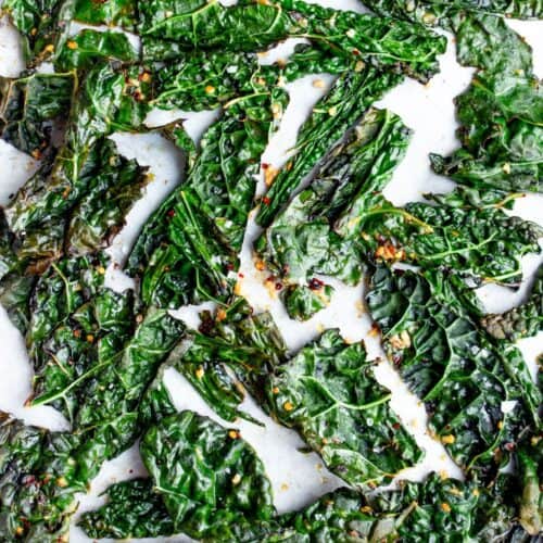 Baked torn pieces of cavolo nero on parchment paper on a baking tray.