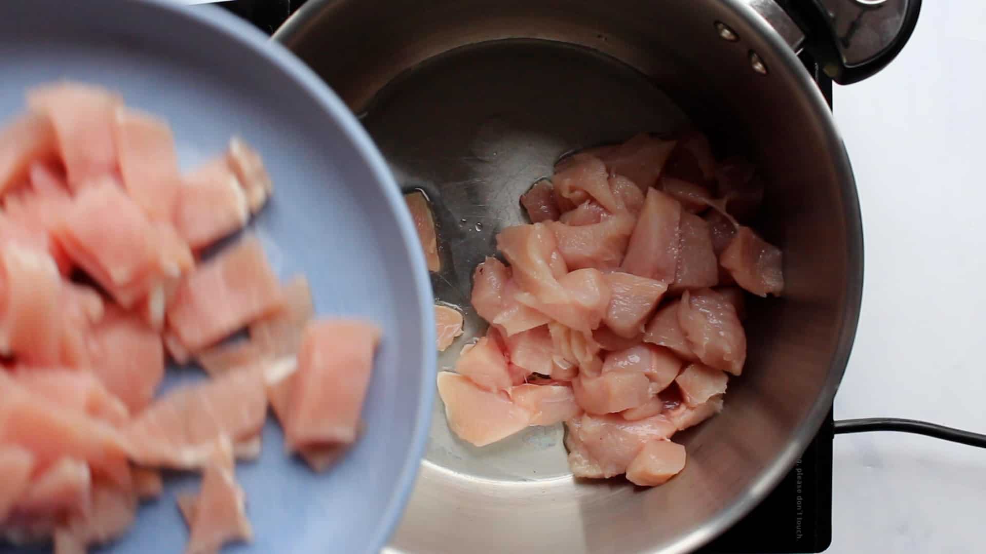 Bacon pieces in a blue bowl added with chicken in a saucepan on the stove.