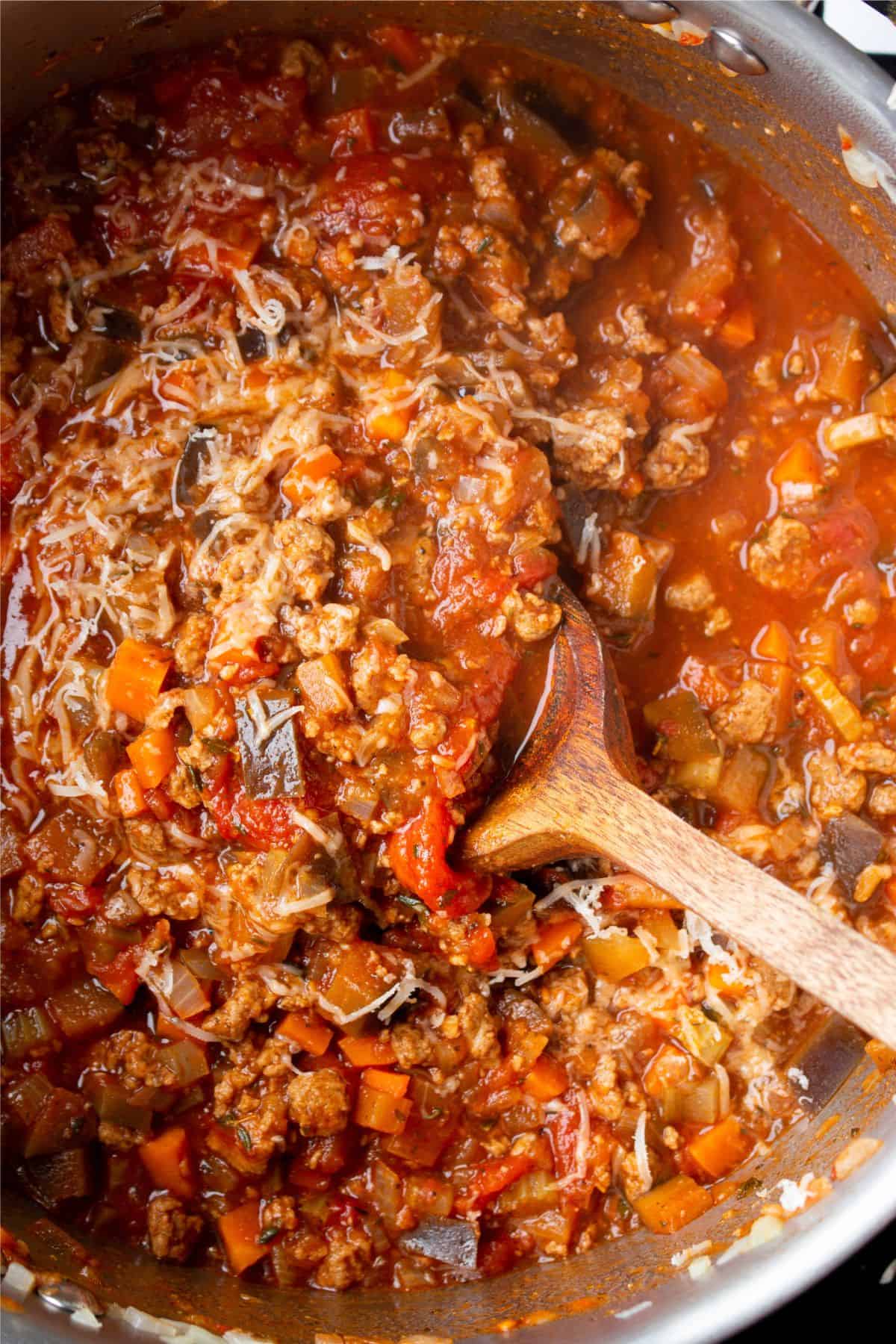 Close up with vegetables and mince mixed in saucepan with a wooden spoon stirring the bolognese.