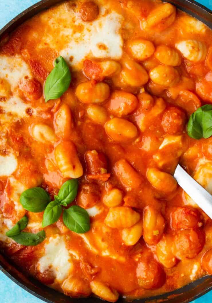 Gnocchi with tomato sauce and mozzarella in large pan with a serving spoon and topped with fresh basil