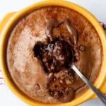 Choclate cake in ramekin with choclatey middle oozing out with spoon.