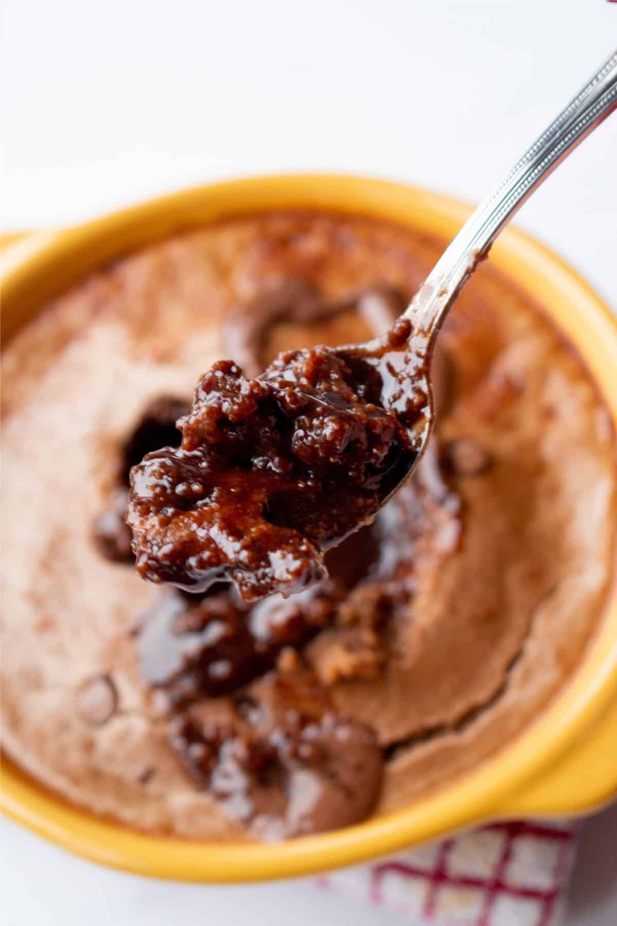 Close up of goey chocolatey cake in a ramekin with a spoon in the middle with the choclate centre.