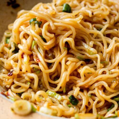 close up of chili oil noodles on a plate with spring onions.