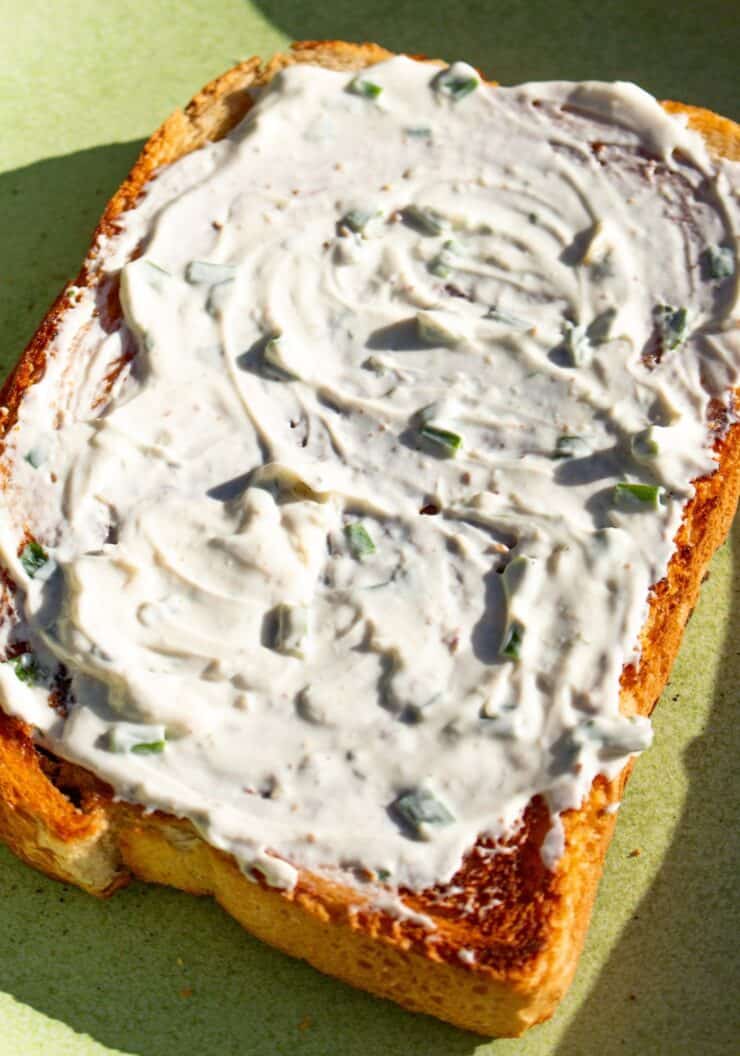A slice of bread with cream cheese spread over in a sunny photo on a green plate.