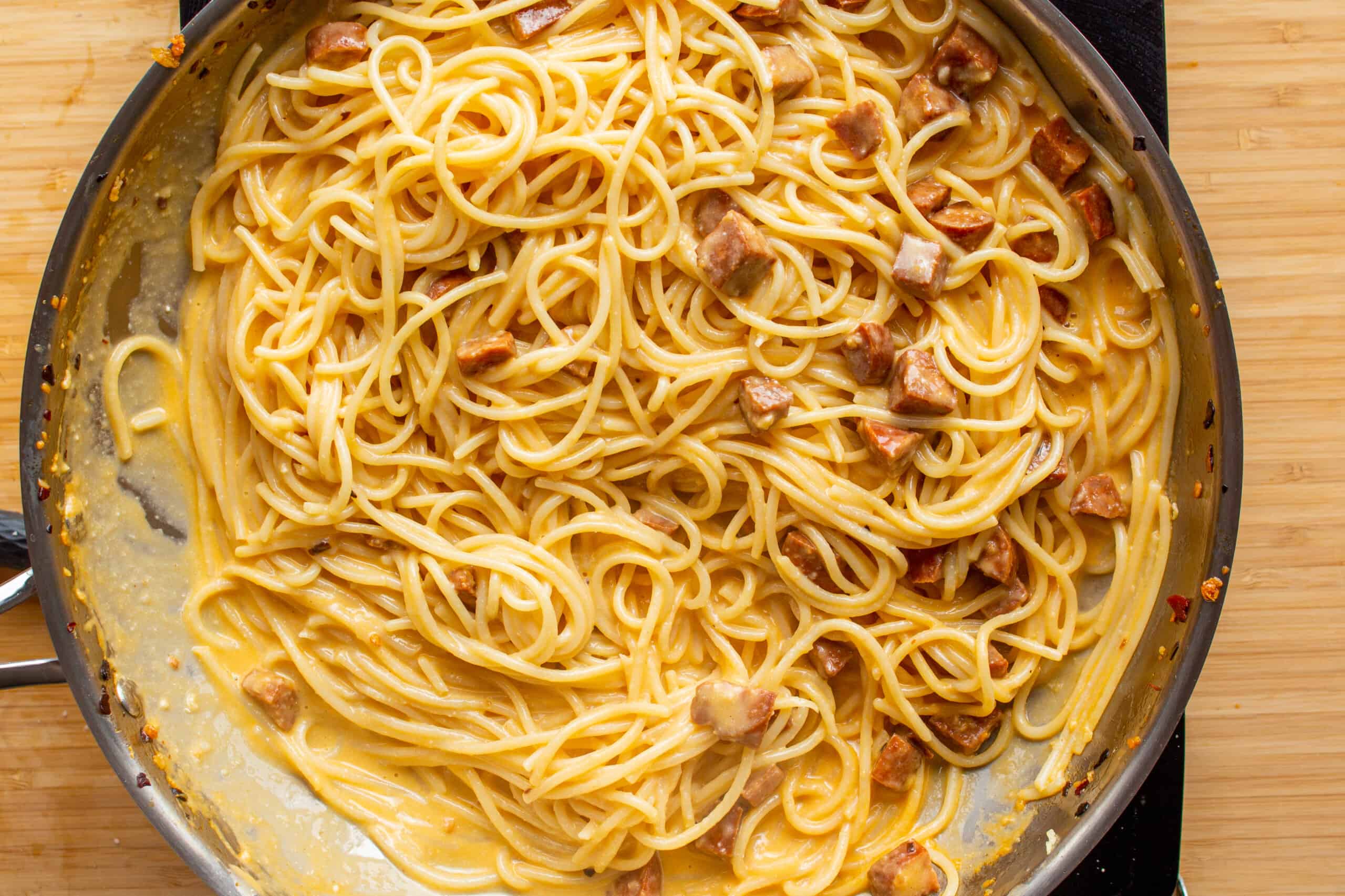 Chorizo carbonara with spaghetti, small slices of chorizo and eggy carbonara sauce in a large stainless steel pan on a stove.