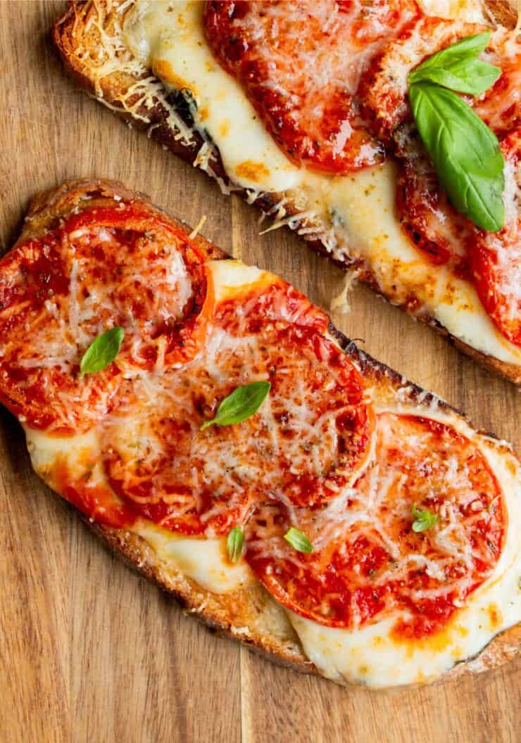2 slices of pizza toast with meted cheese and fresh basil on a wooden board.