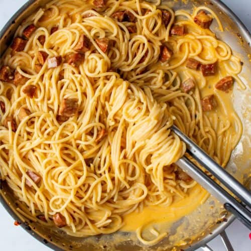 A large stainless steal pan filled with spaghetti, chorizo and carbonara sauce.