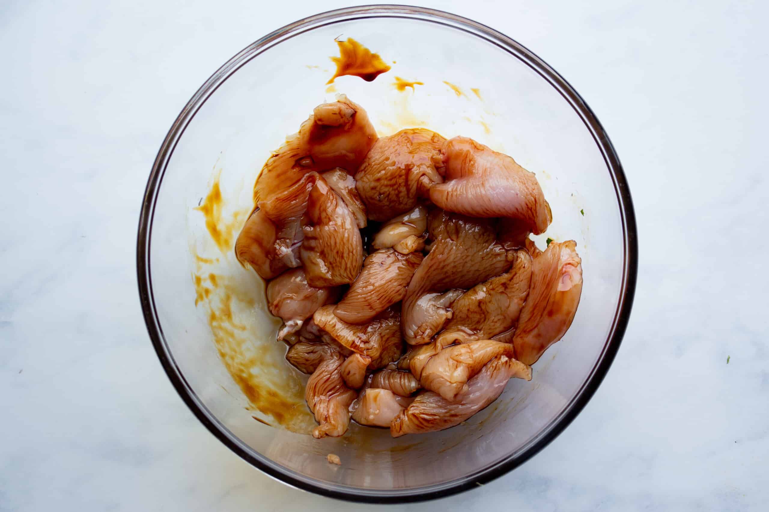 Chicken pieces marinated in the soy sauce in a glass bowl.