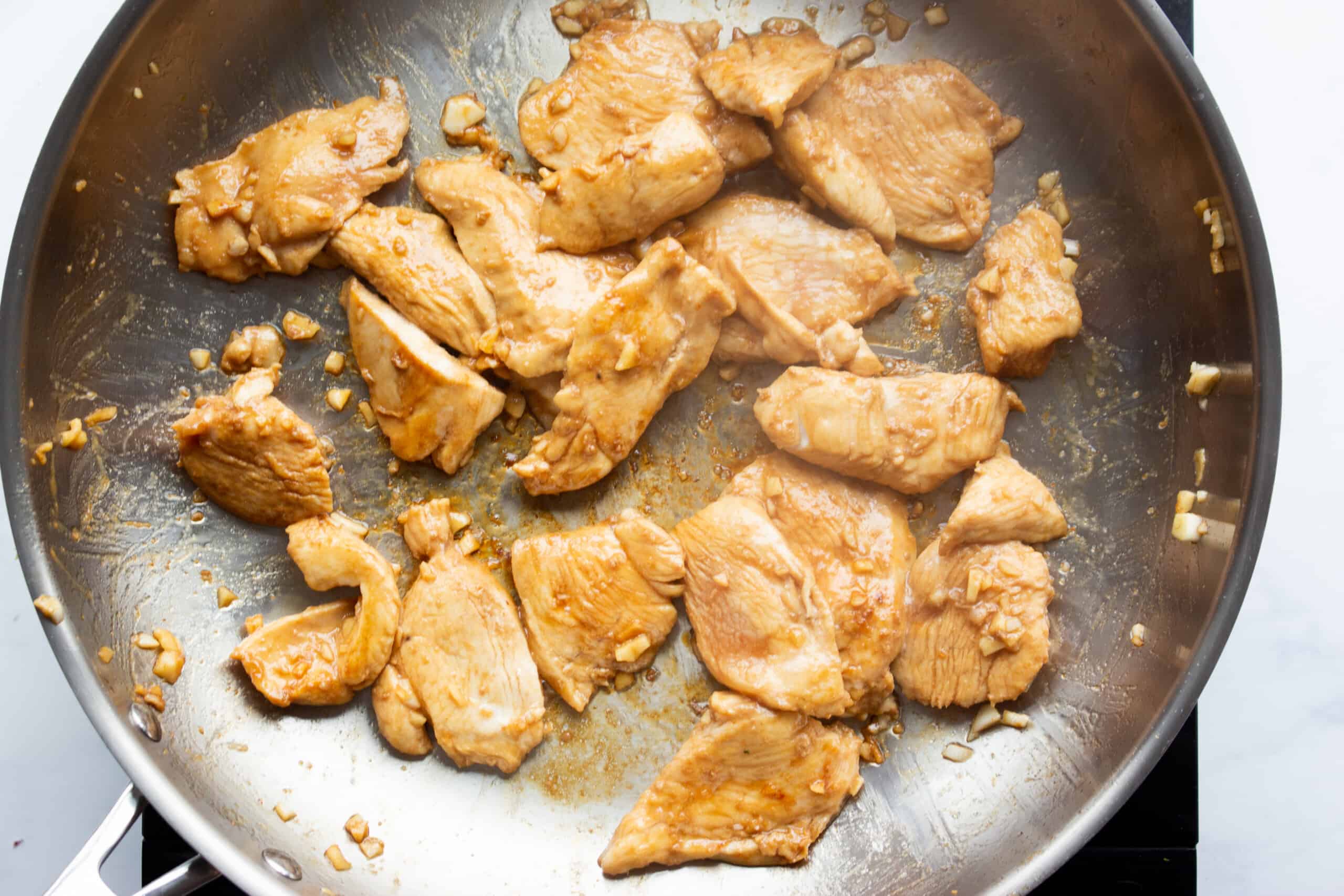 Marinated chicken pieces frying in a stainless steel pan.