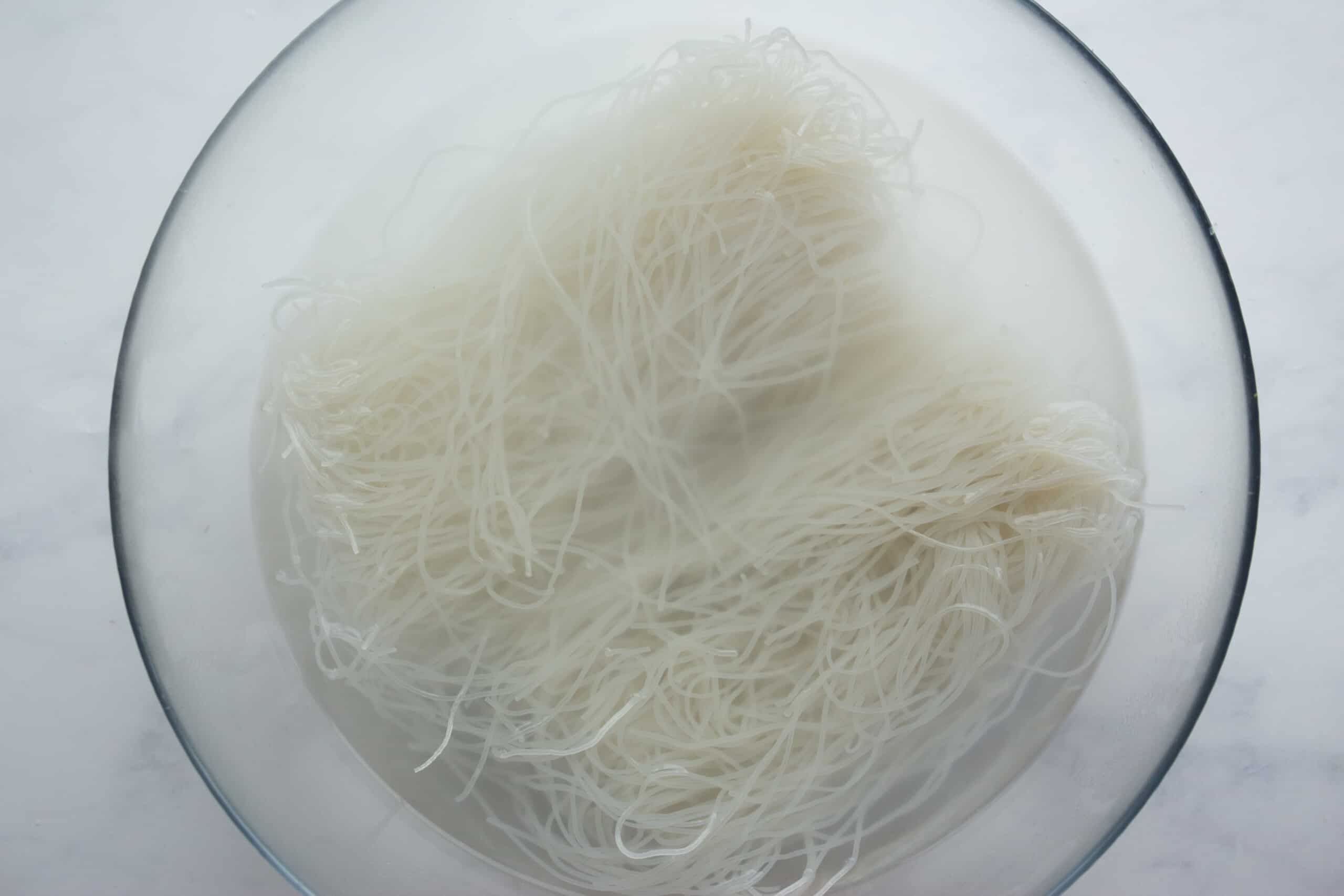 Vermicelli noodles in boiling water in a large glass bowl.