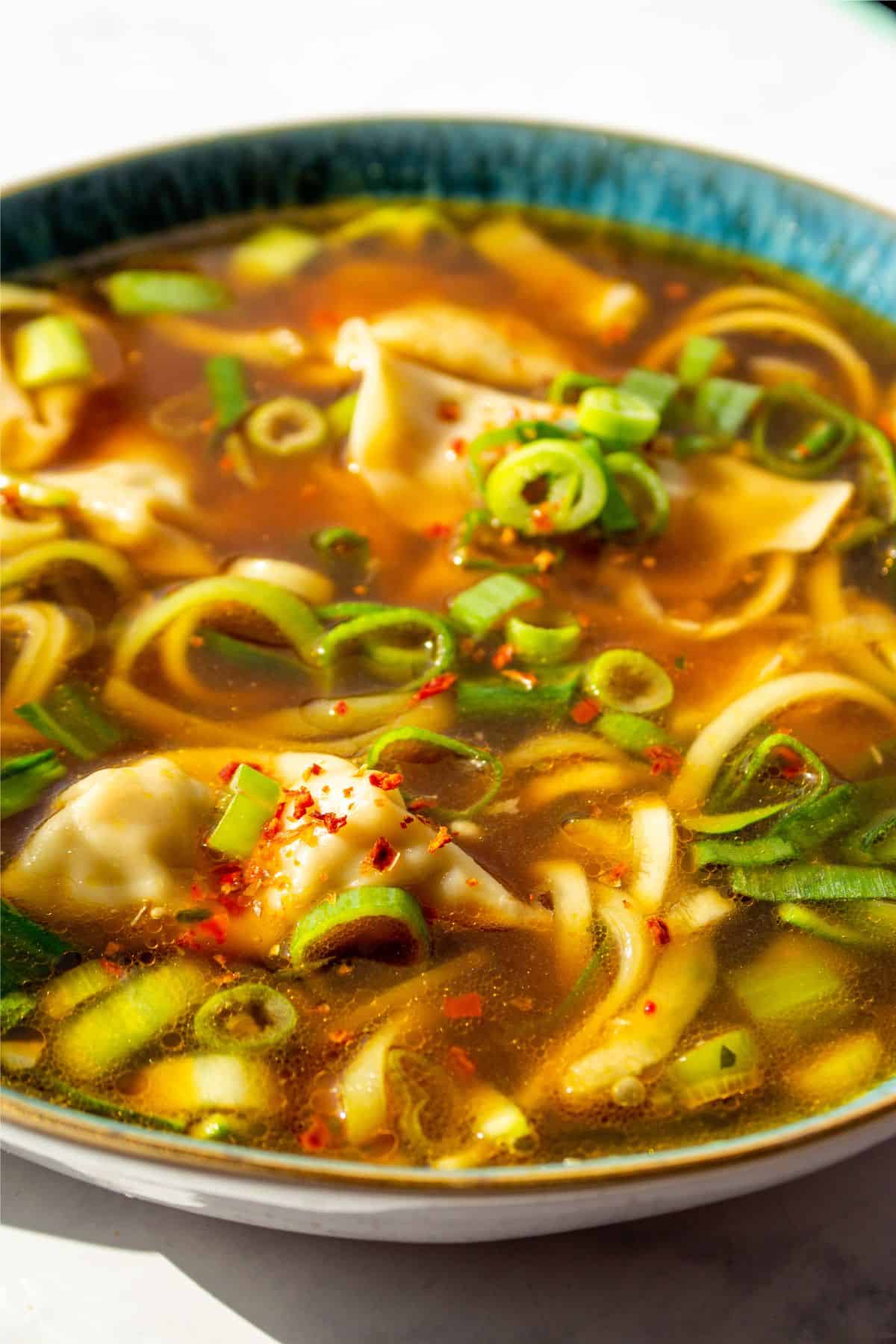 Close up of soup with dumplings, spring onions, pok choi and spiralised courgette. 