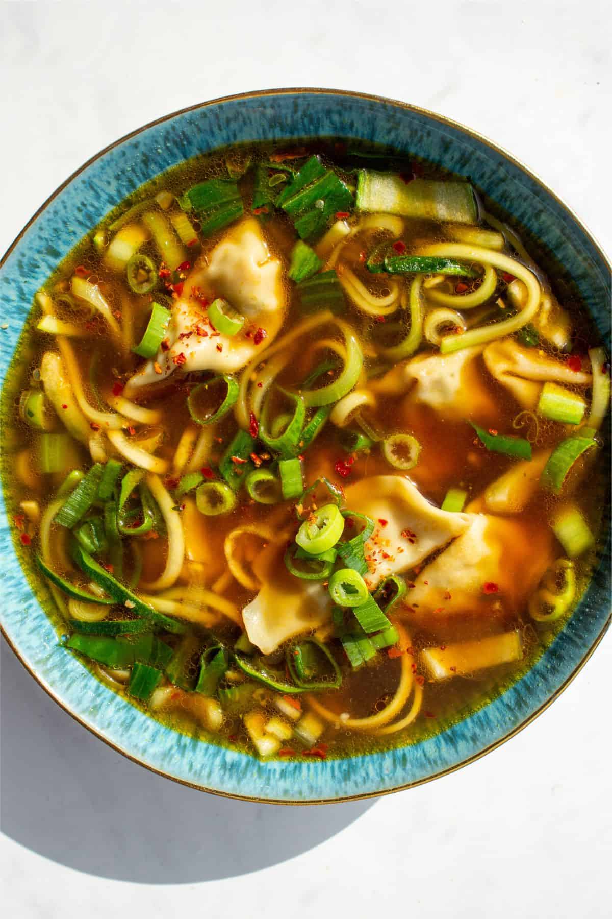 A blue bowl with soup with dumplings, spring onions, pok choi and spiralised courgette.