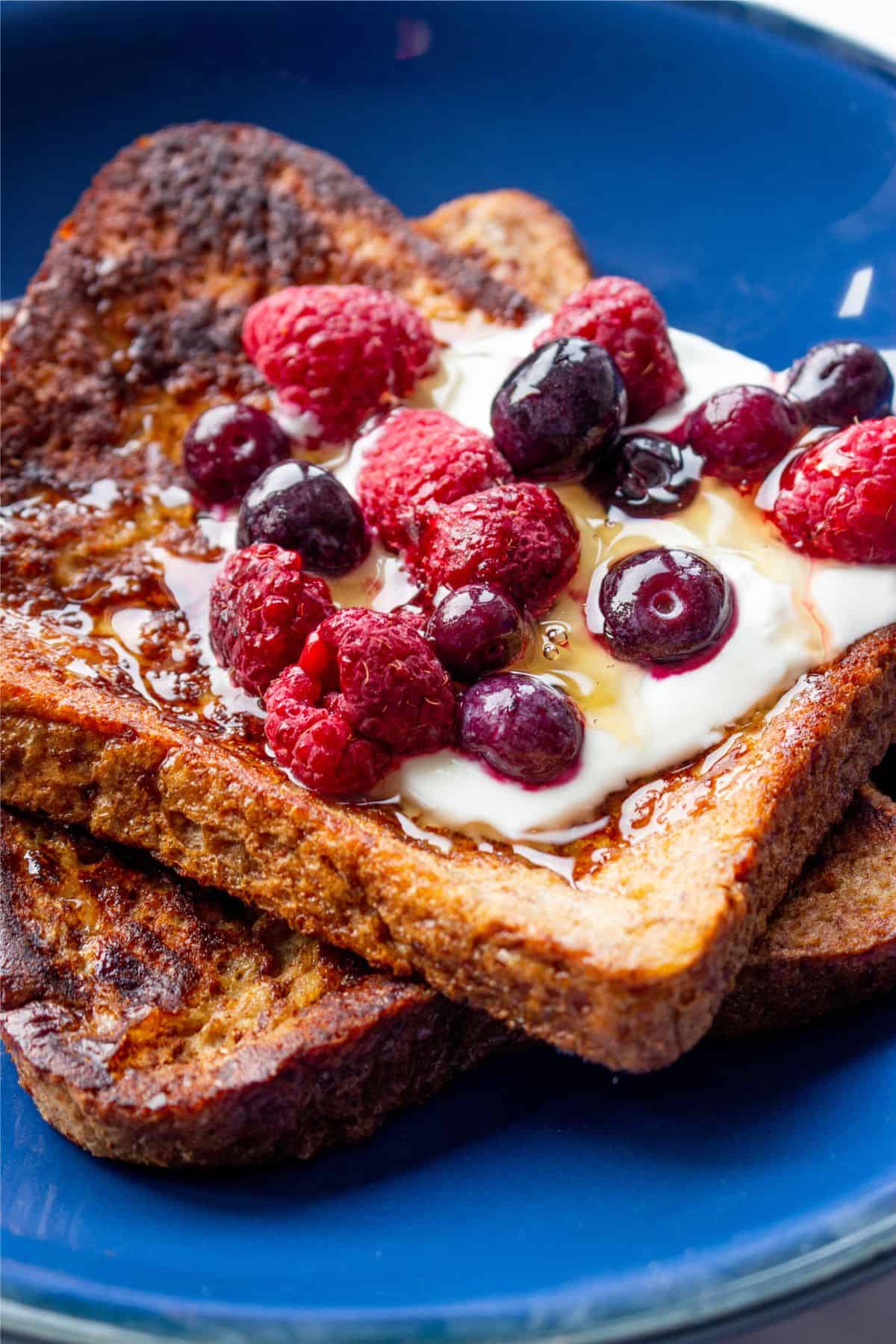 Close up of 2 slices of cinnamon French toast in a blue bowl with yogurt, honey and mixed berries.