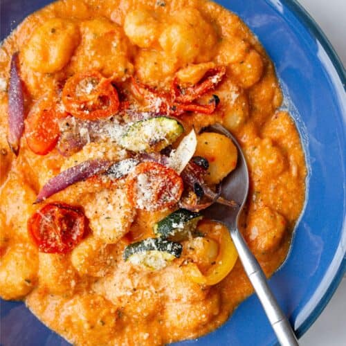 A bowl of gnocchi with tomatoey creamy sauce and roasted vegetables topped with parmesan.