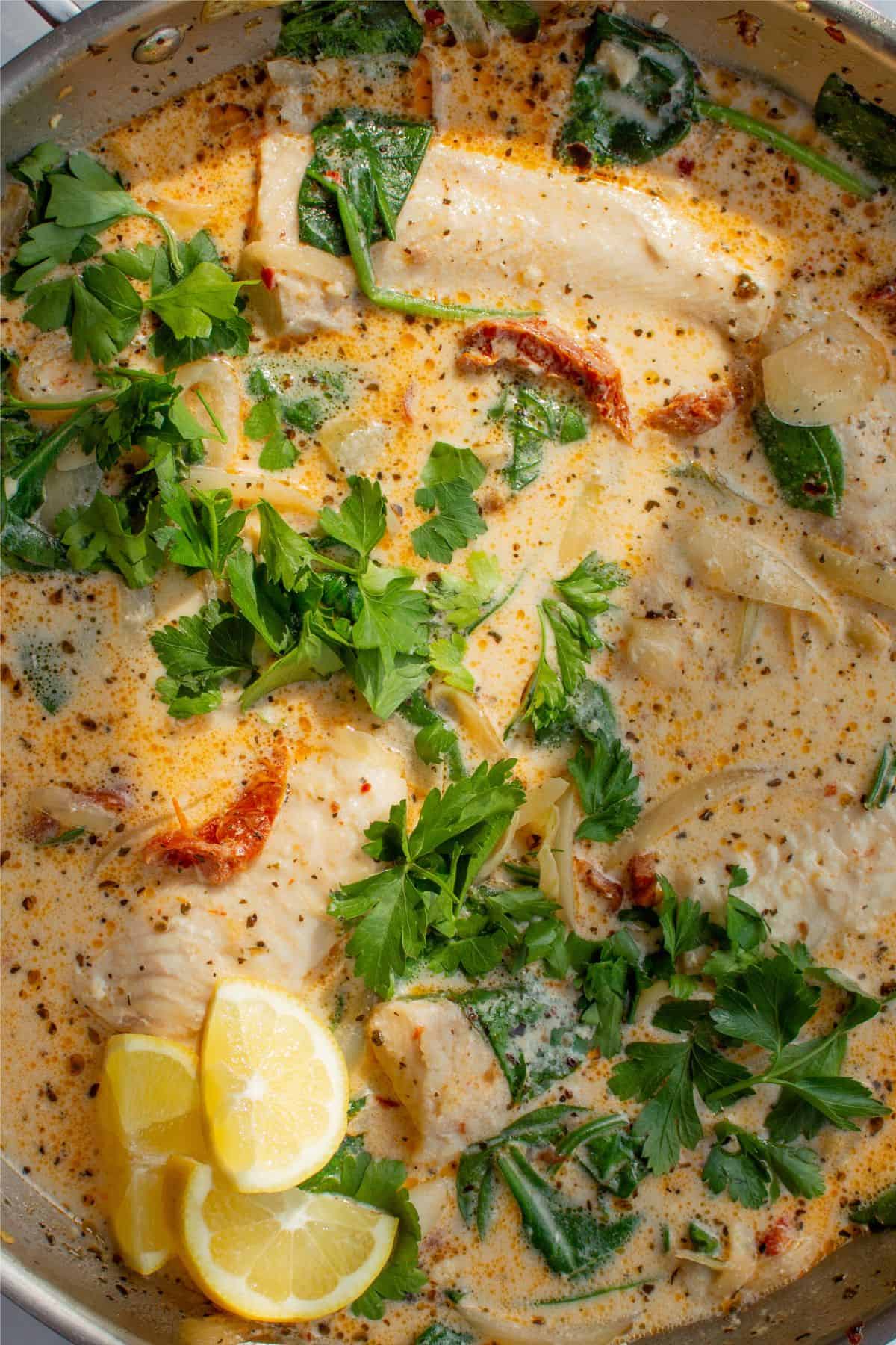 Close up of creamy sauce with basa fillets and parsley and lemon wedges.