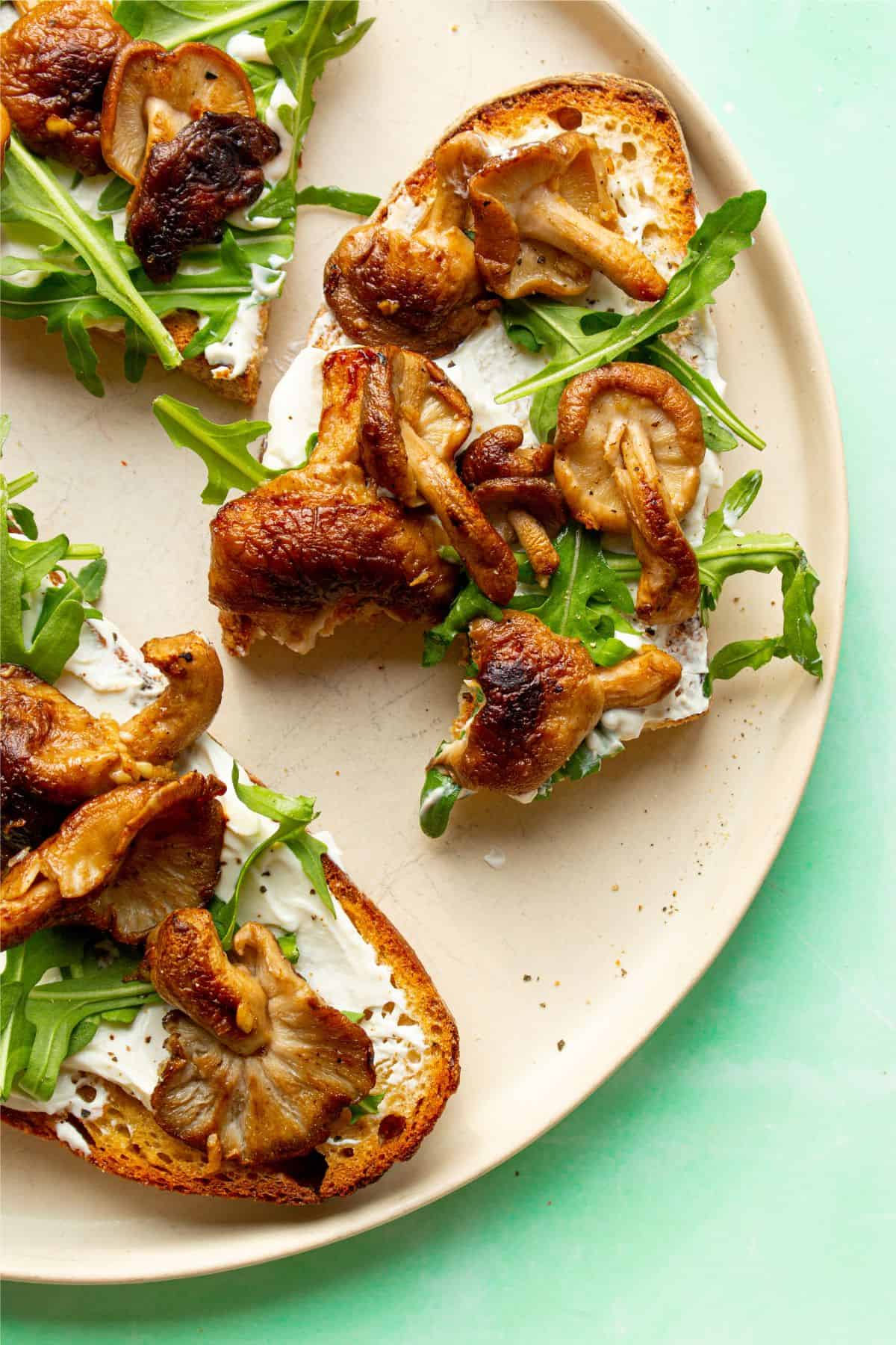 Creamy mushroom toast with cream cheese, browned mushrooms and rocket on a plate with a bite taken from one piece.