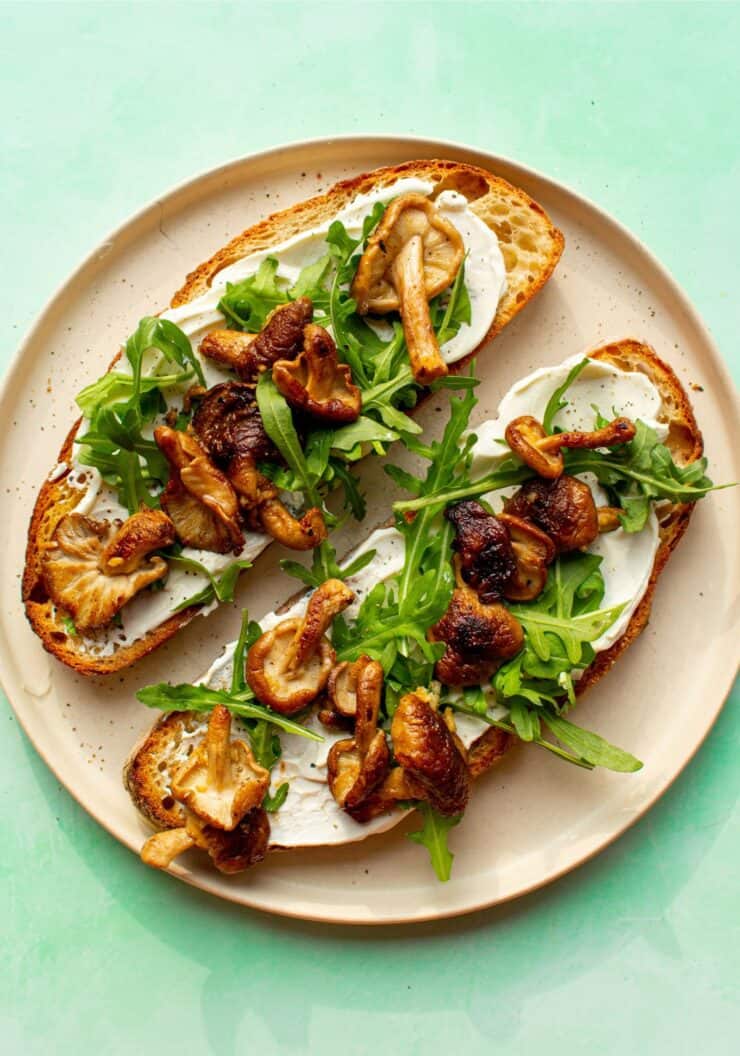 2 slices of sourdough on a plate topped with cream cheese, browned mushrooms and rocket.