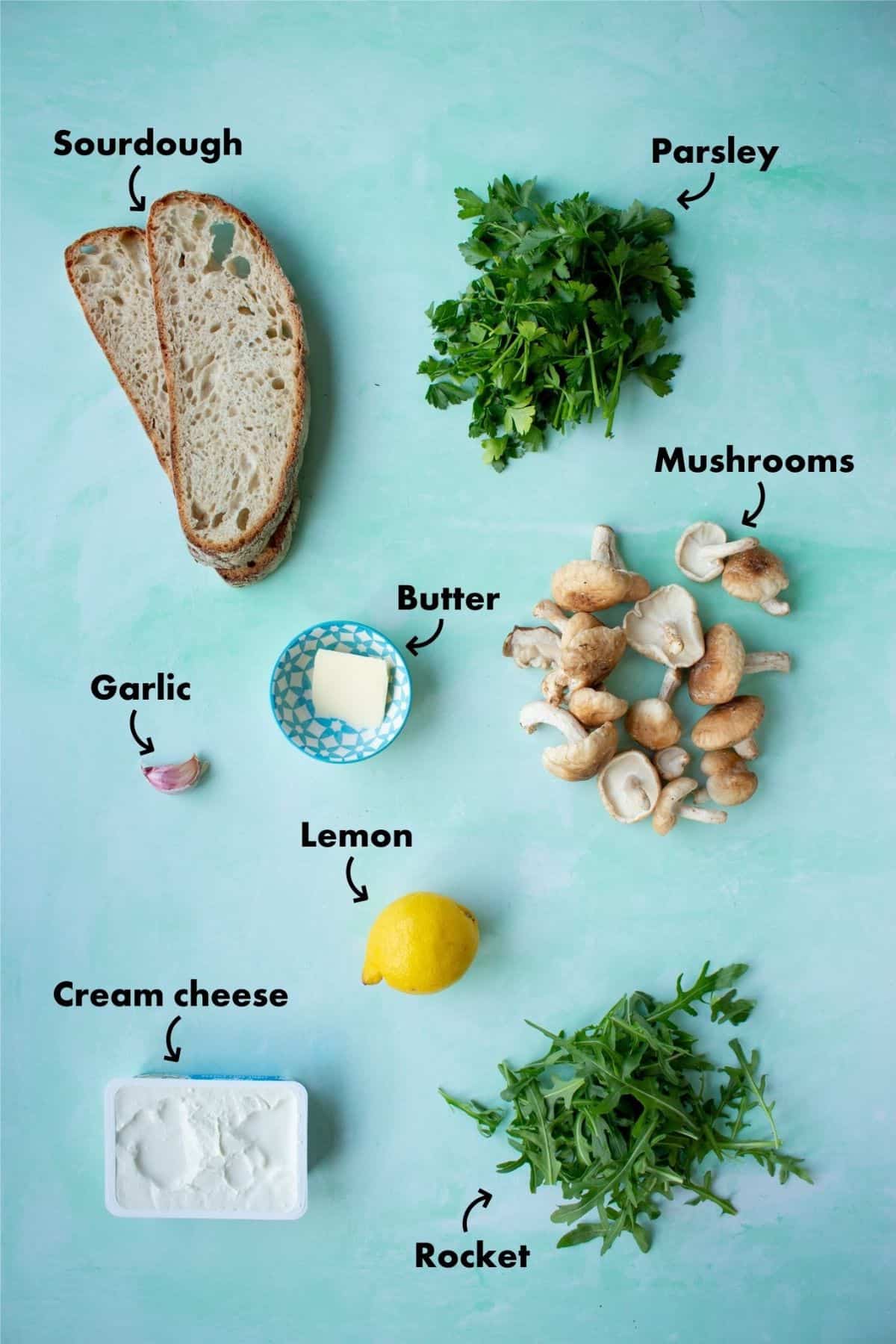 Ingredients to make mushroom toast laid out on a pale blue background and labelled.