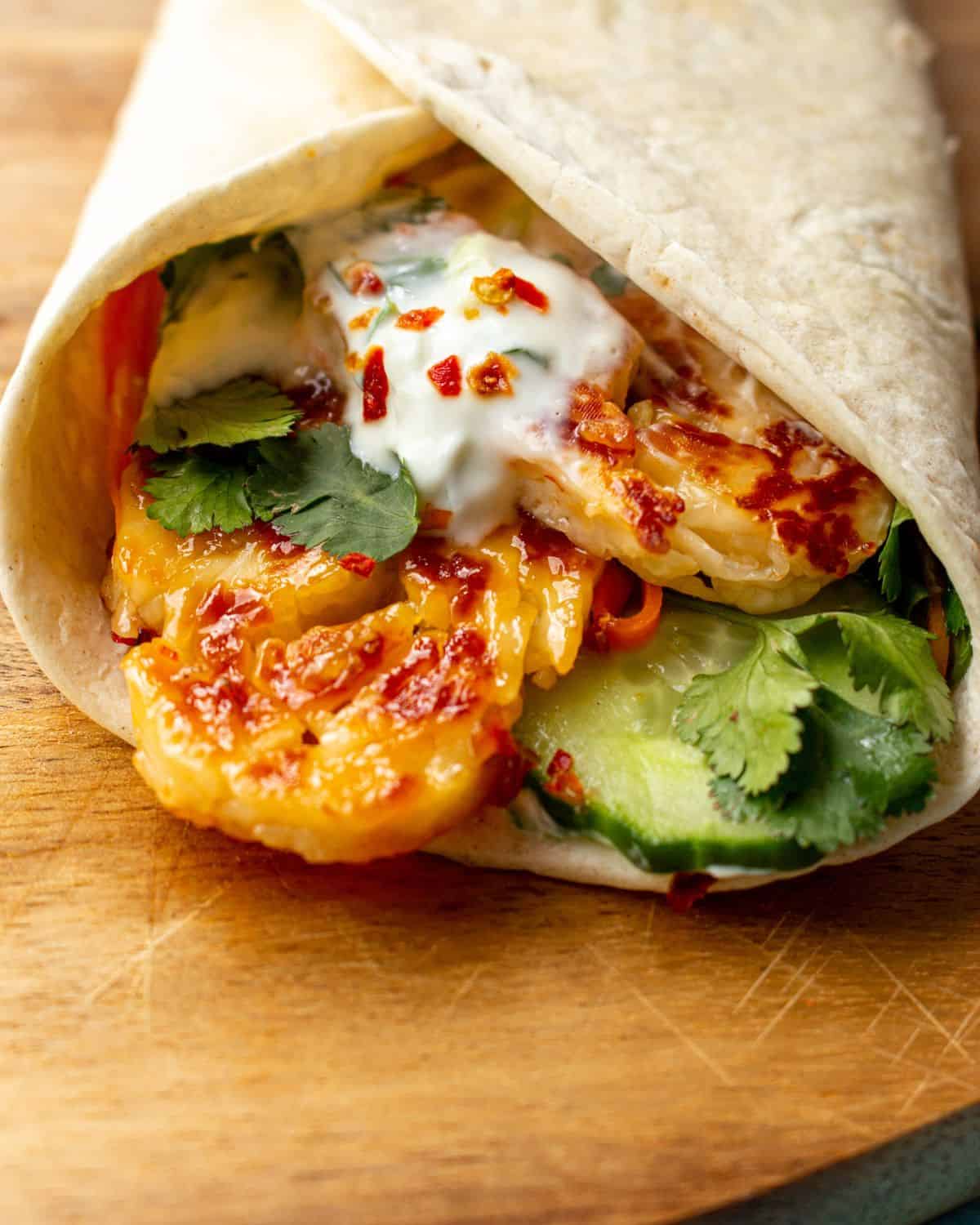 Wrap folded over and filled with golden browned halloumi, cucumber, lettuce and Tzatziki on a wooden board.