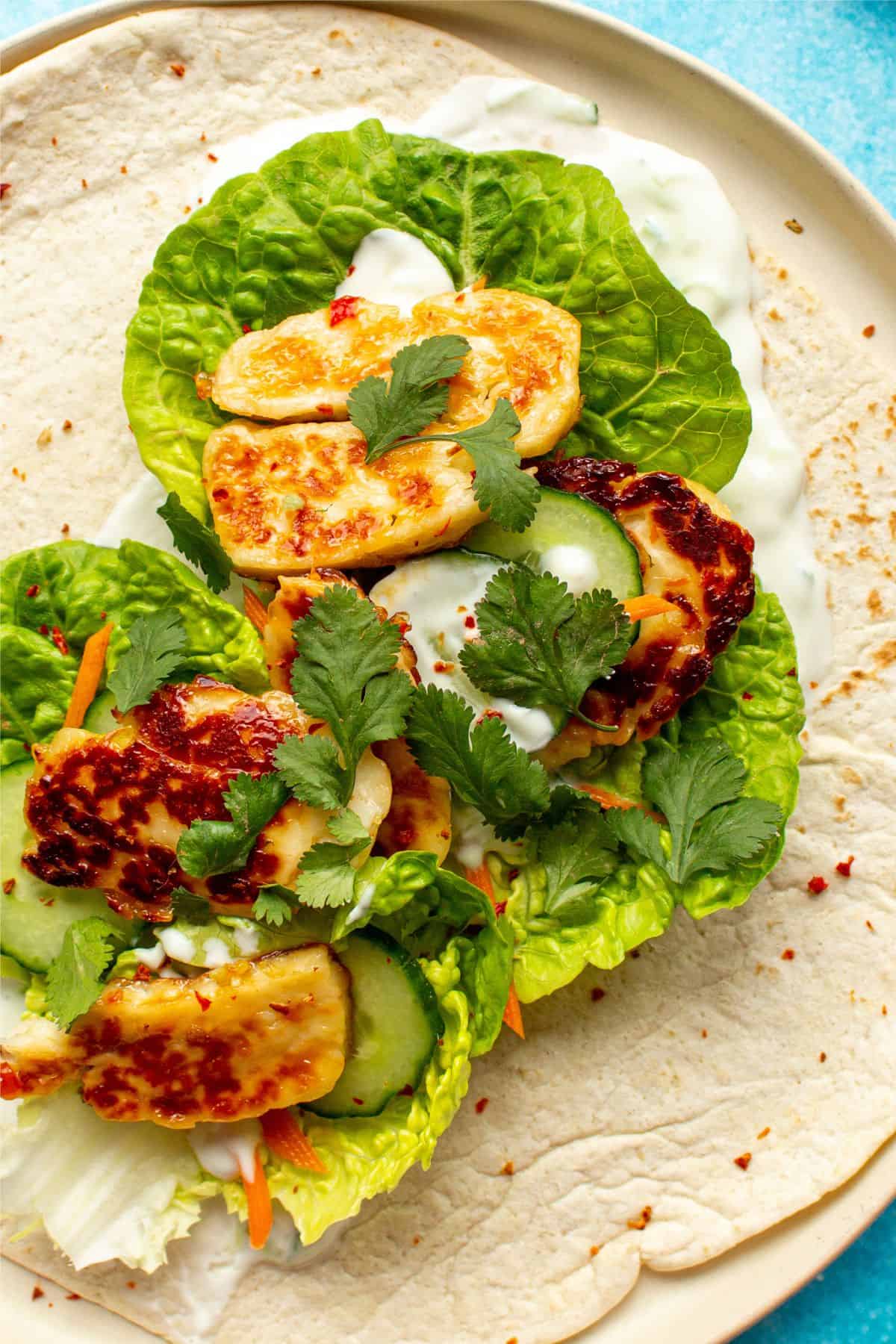 close up of a Halloumi Wrap with cucumber, carrots browned halloumi, lettuce and Tzatziki.