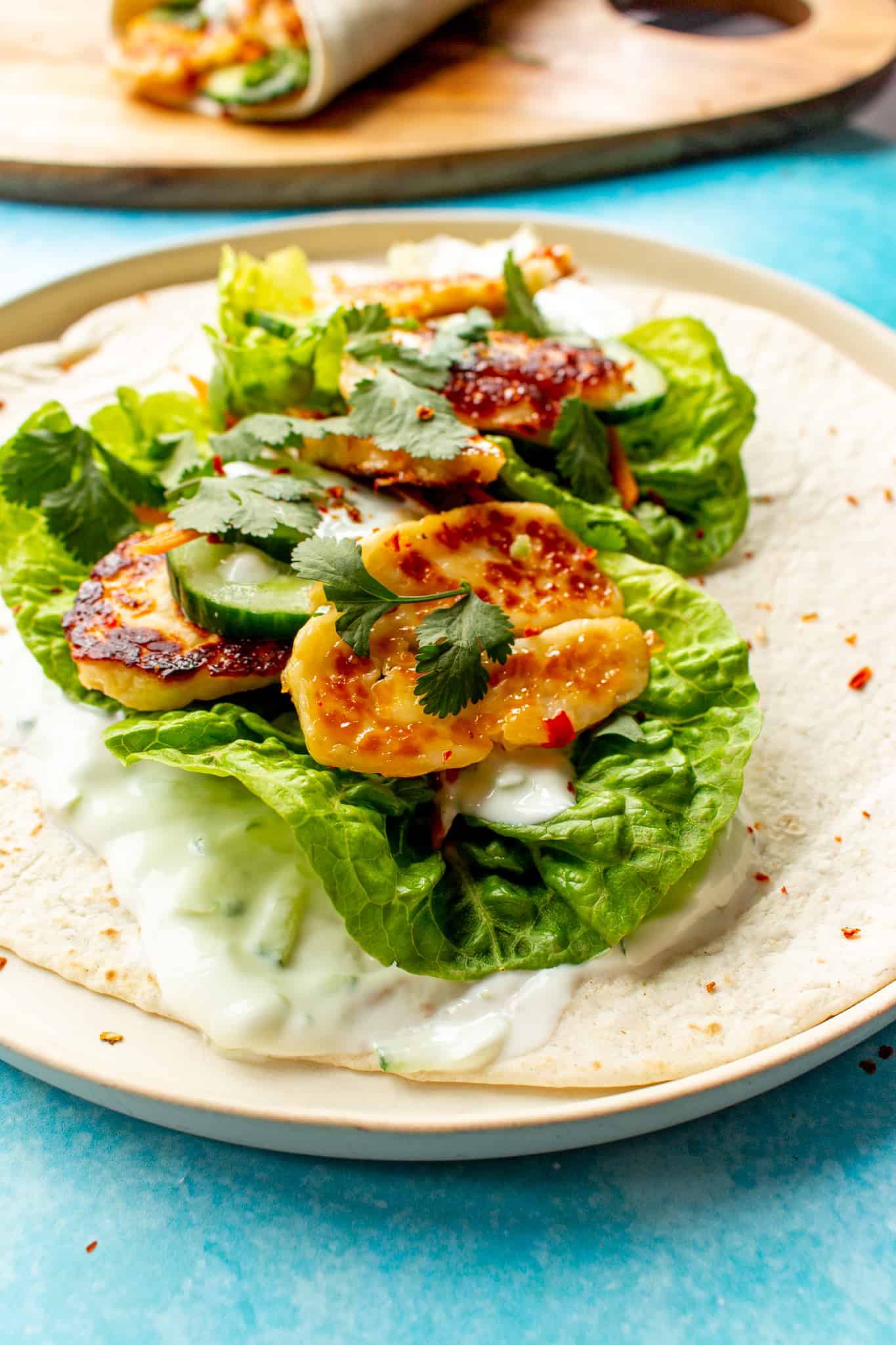 Close up of a sweet chilli halloumi wrap on a plate with lettuce, carrot, halloumi and topped with the sweet chilli and Greek yogurt.