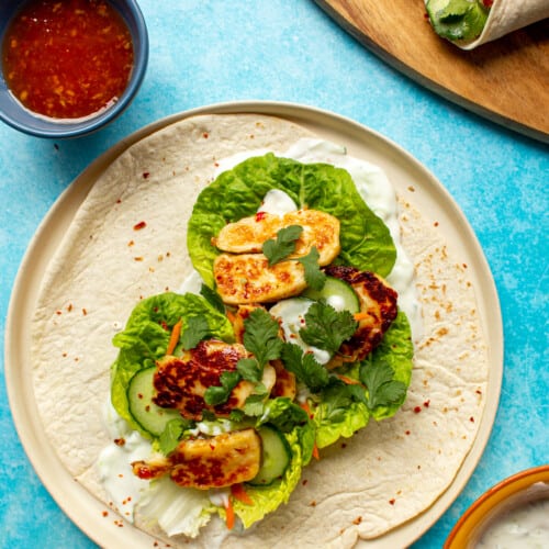 A Sweet Chilli Halloumi Wrap on a plate with lettuce, carrot, halloumi and topped with the sweet chilli and Greek yogurt (in 2 bowls).