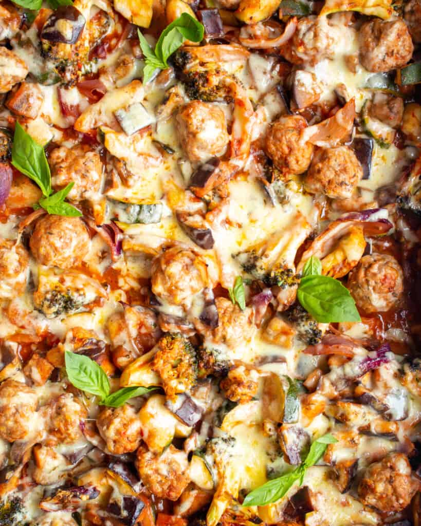 Close up of Baked Turkey Meatballs with Saucy Roasted Vegetables topped with melted cheese and fresh basil.