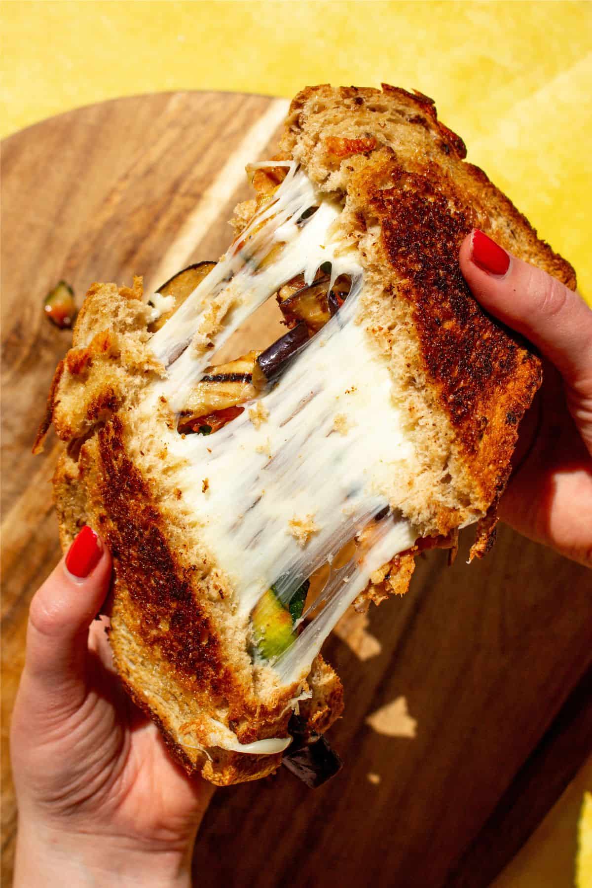 Pulling sandwich apart with 2 hands showing mozzarella cheese pull.