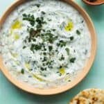 Tzatziki in a bowl topped with mint and oil with partial view of naan bread.