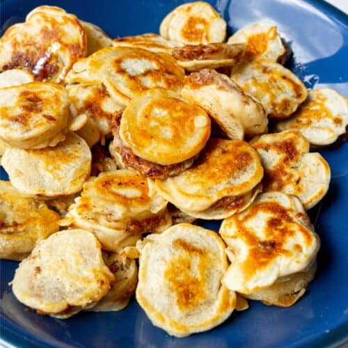 A blue bowl filled with mini golden, browned pancakes with filling.