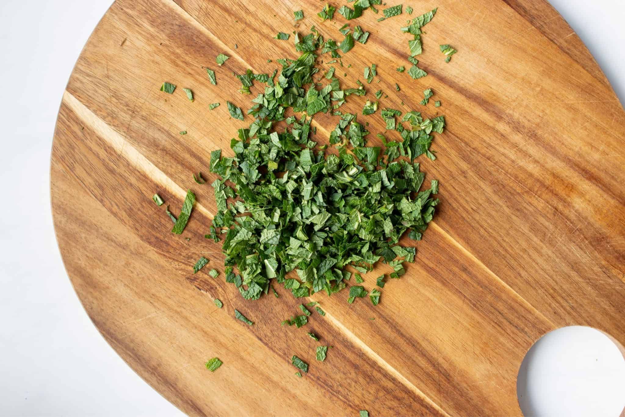 Finely chopped mint on a wooden oval chopping board.