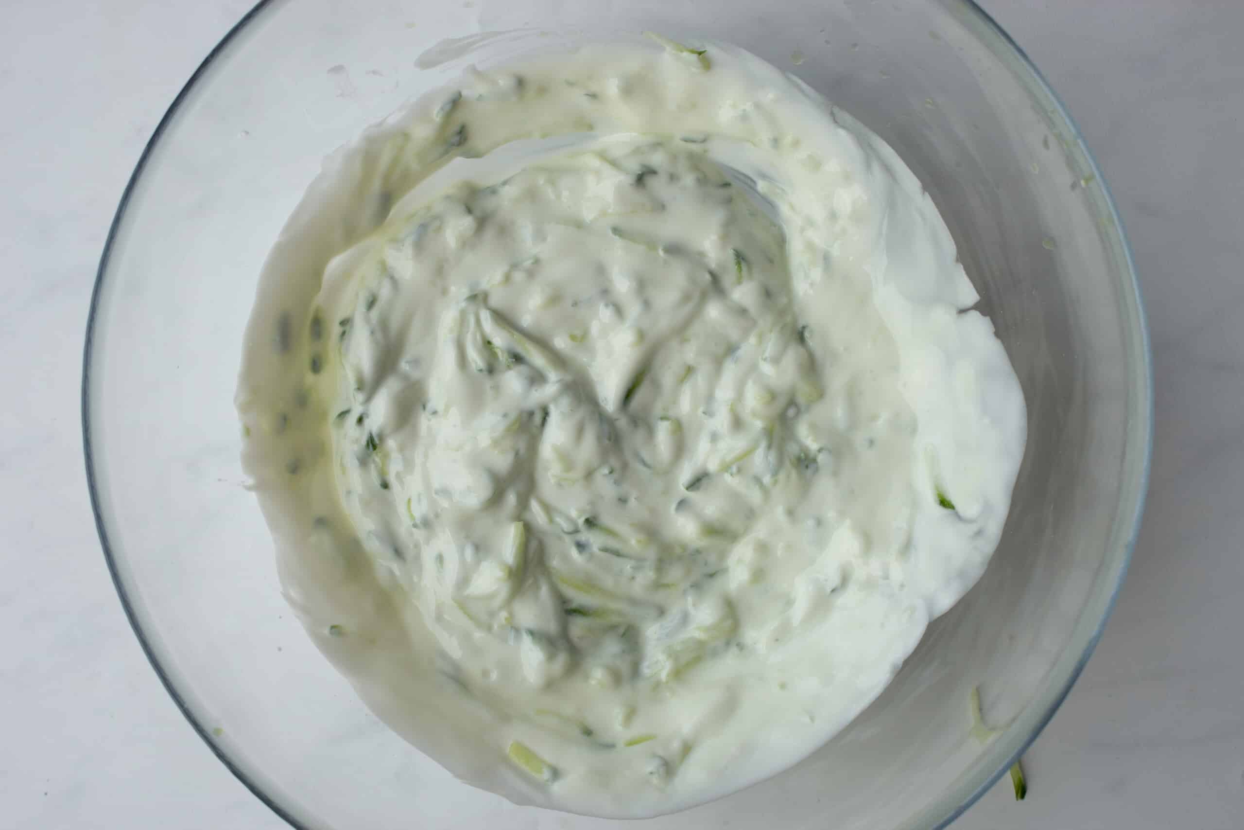 Grated cucumber and yogurt mixed together in a large glass bowl.