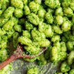 Close up of gnocchi in a pan with green pesto and mixed with a wooden spoon.