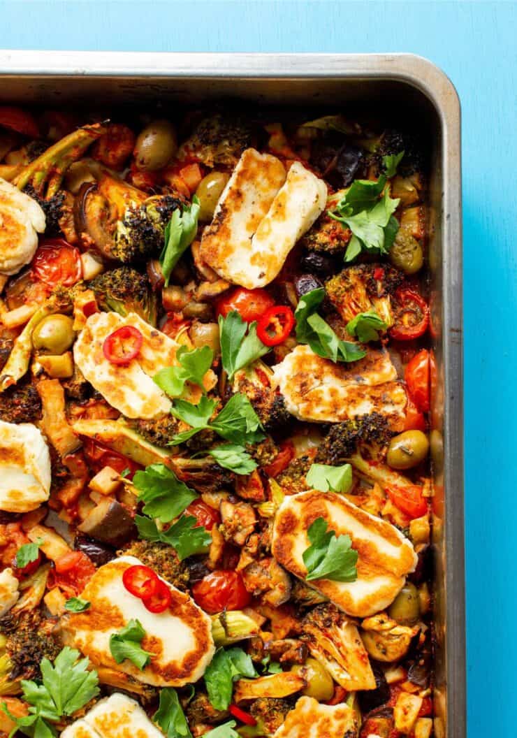 Roasted vegetables in a tray topped with golden browned halloumi and coriander.
