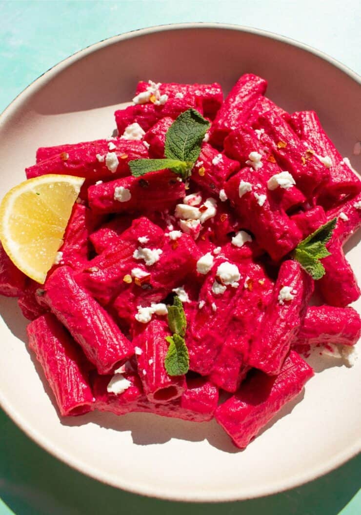pink pasta in a bowl with a lemon wedge and topped with some feta.