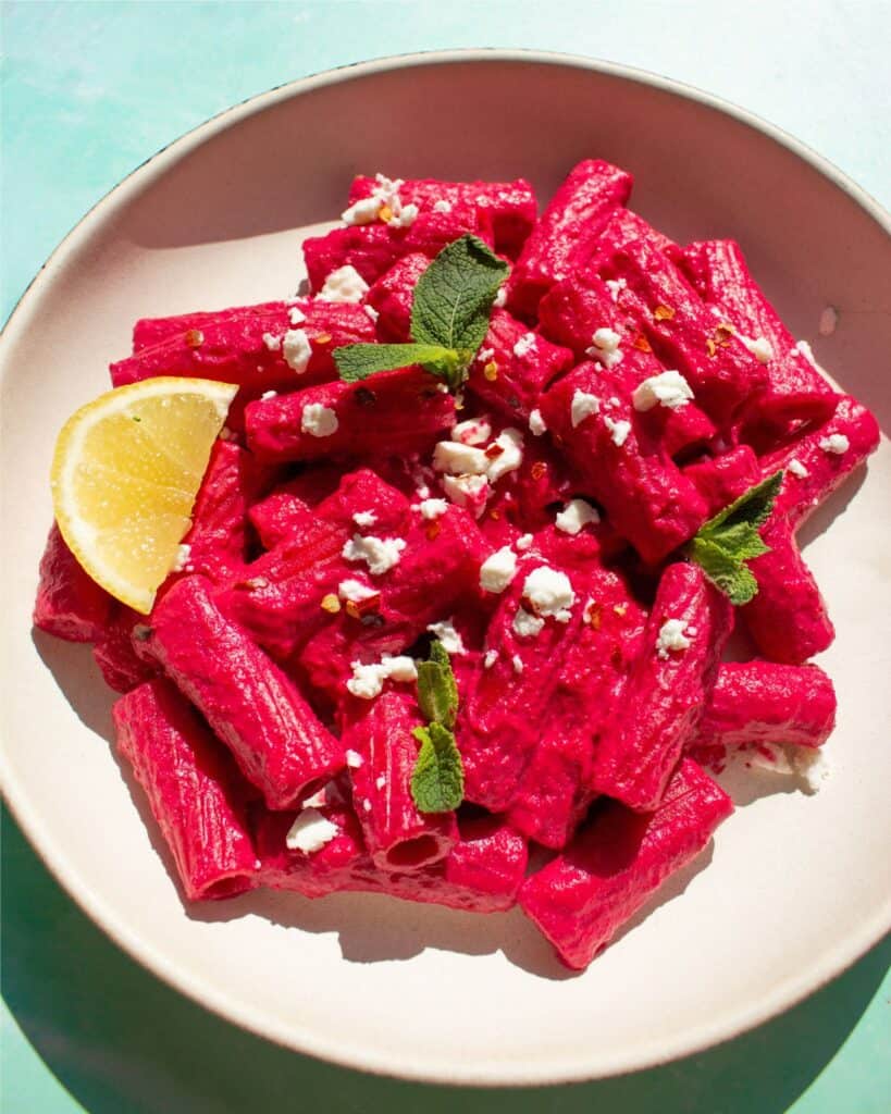 pink pasta in a bowl with a lemon wedge and topped with some feta.