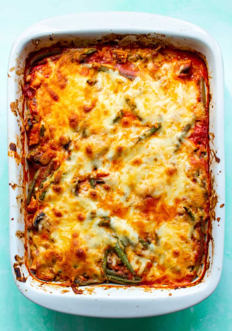 Cheesy Baked Tomato Rice with Chicken & Veg with golden brown cheese topping in a white rectangular baking dish on a pale blue background.