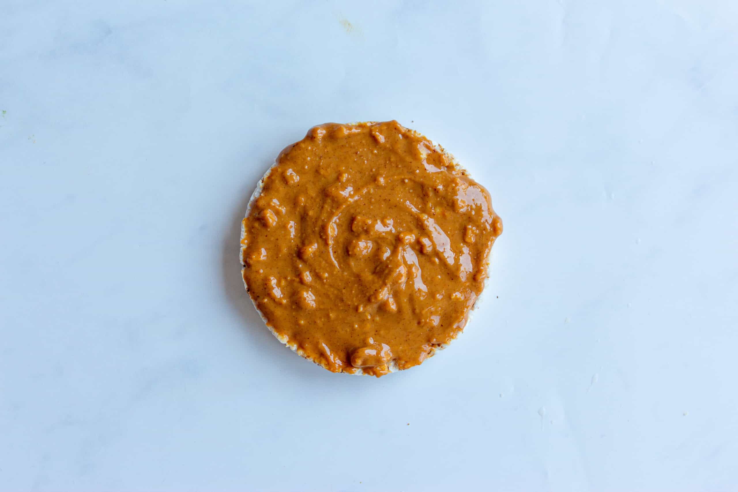Peanut butter spread over the plain rice cake on pale white background.