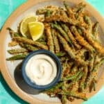 Golden browned green beans on a palte with some mayonaise in a small blue bowl.