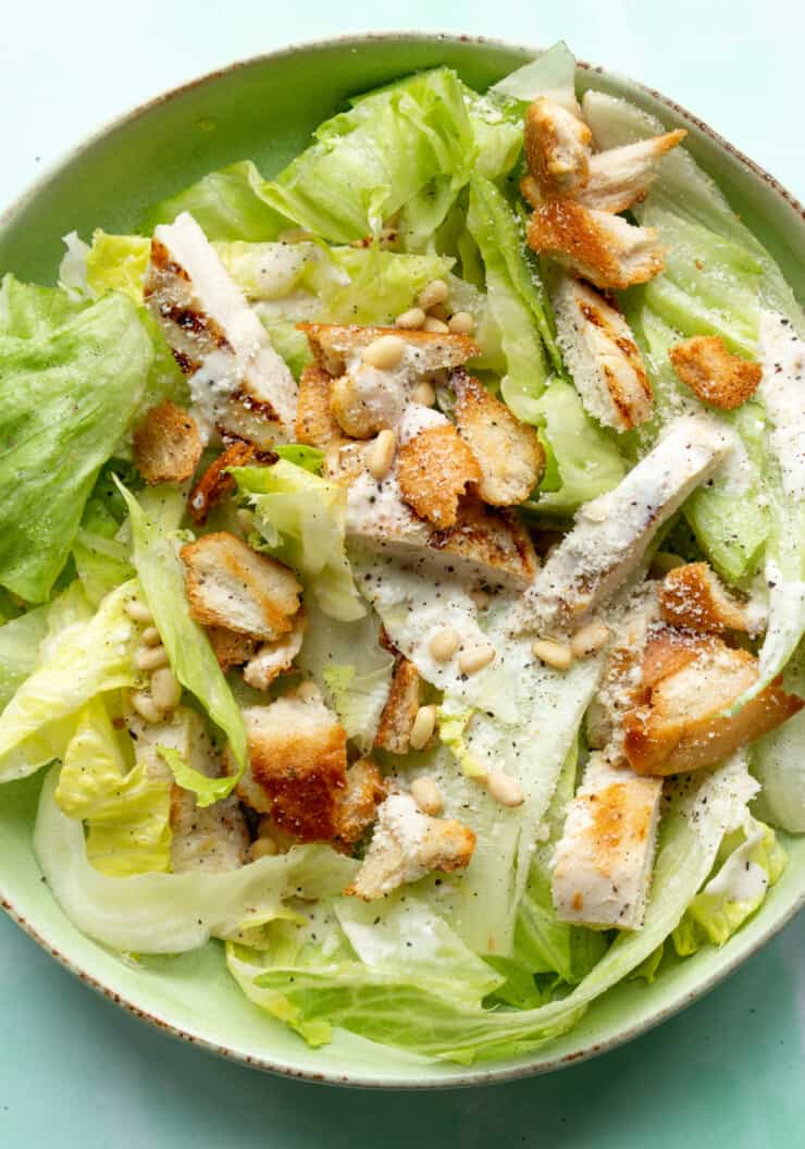 Chicken Caesar Salad on a bed of lettuce with chicken slices, parmesan and croutons topped with pine nuts and Caesar dressing.
