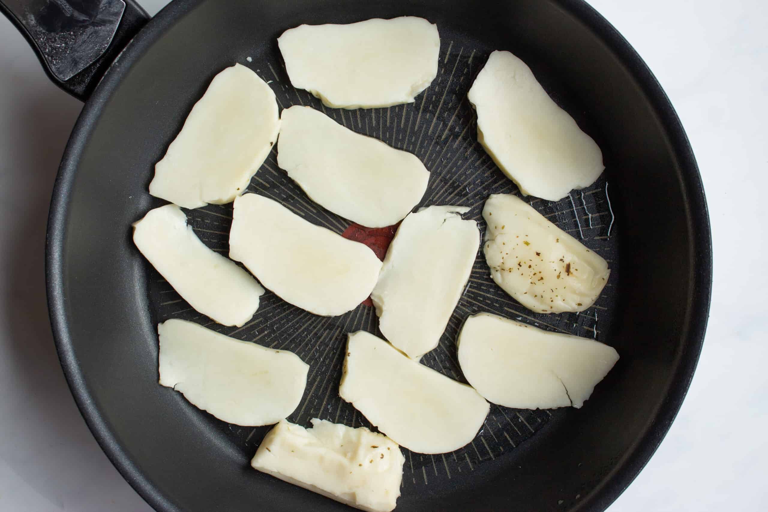 Thinly sliced halloumi in a black frying pan.