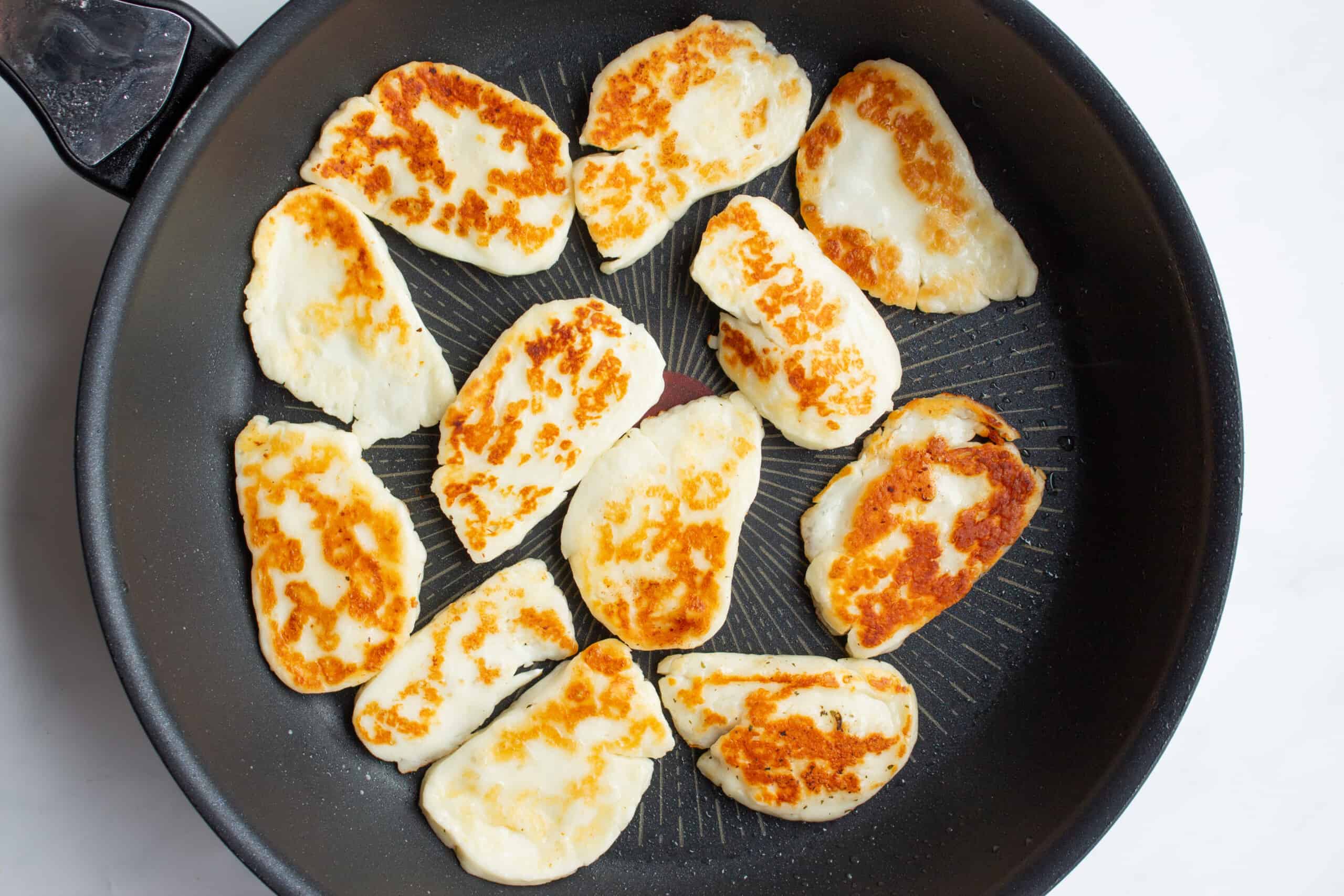 Golden browned halloumi slices fried in a black pan.