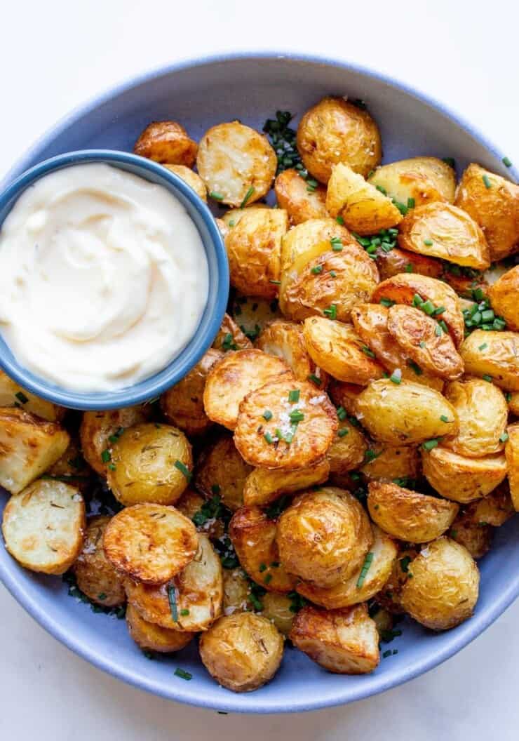 Air Fryer new potatoes in a blue bowl garnished with chives and served with dipping sauce.