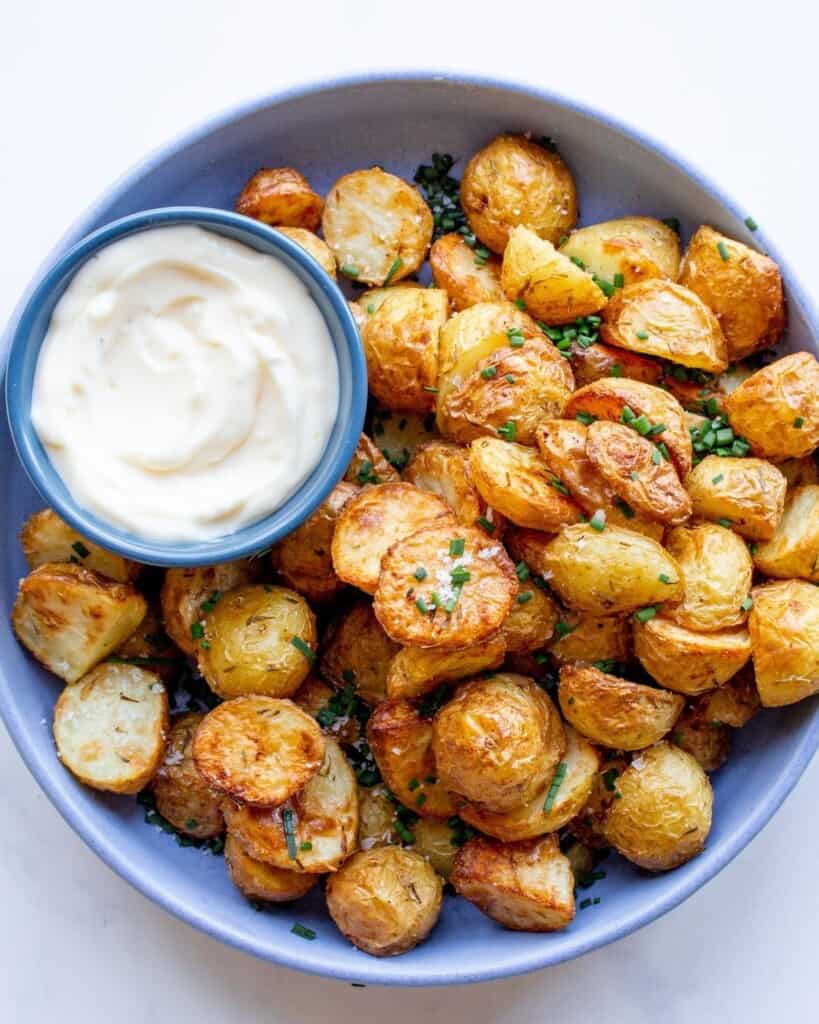 Air Fryer new potatoes in a blue bowl garnished with chives and served with dipping sauce.