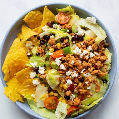 Dorito taco salad in a bowl with browned mince, tomatoes, lettuce, Doritos and crumbled feta.