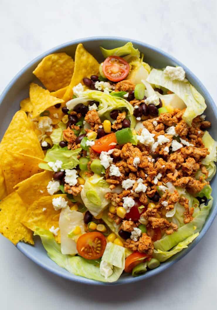 Dorito taco salad in a bowl with browned mince, tomatoes, lettuce, Doritos and crumbled feta.