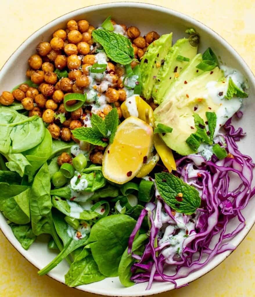 Avocado & Chickpea Nourish Bowl with red cabbage, roasted chickpeas, sliced avocados on a bed of spinach with lemon, mint and dressing.