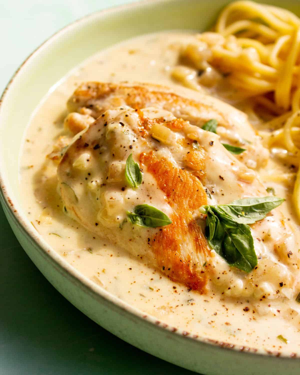 Close up of Philadelphia chicken served with spaghetti and garnished with fresh basil.