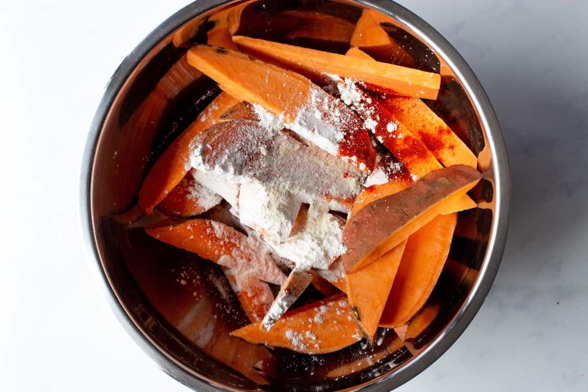 Sweet potato wedges in bowl with cornflour and seasoning